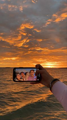 a person holding up a cell phone to take a photo with the sunset in the background