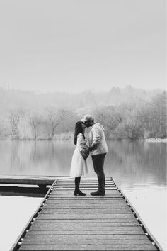 a couple kissing on the end of a pier in front of a body of water