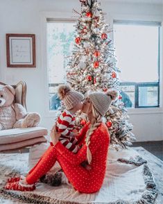 two women sitting on the floor in front of a christmas tree wearing knitted hats