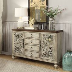 a white dresser sitting in front of a painting on the wall next to a lamp