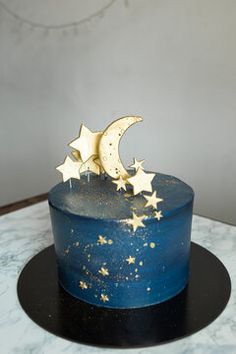 a blue cake with gold stars and moon decorations on top, sitting on a black plate