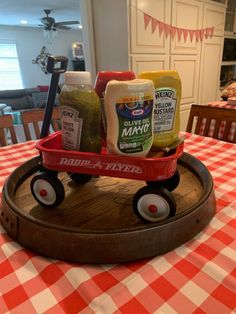 a red wagon filled with condiments on top of a checkered table cloth