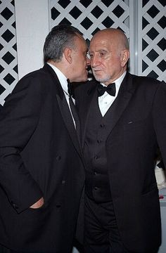 two men in tuxedos are standing next to each other and one is kissing the other