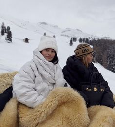 two women sitting on the back of a large stuffed animal in the snow with mountains behind them