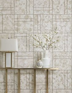 a vase with flowers on a table in front of a wallpapered background that looks like tile