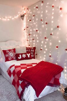 a bedroom decorated in red and white with christmas lights on the wall behind the bed