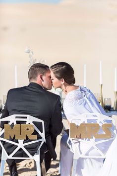 a bride and groom kissing on their wedding day at the beach with candles in the background