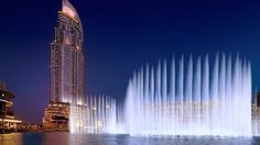 a large fountain in front of a tall building with water shooting from it's sides