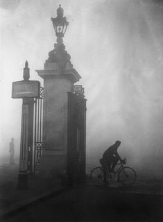 a man riding a bike past a tall blue clock on top of a pole in the fog