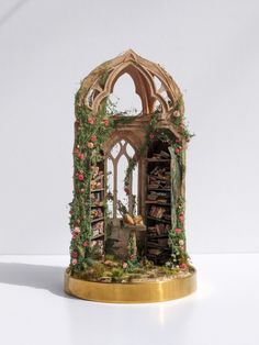 a miniature book shelf with books and plants on it's sides, in front of a white background