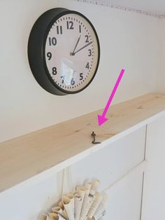 a clock mounted to the side of a wall above a shelf with seashells