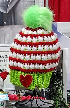 a green and white knitted hat sitting on top of a display stand next to other items