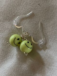 two green earrings with smiley faces hanging from silver earwires on a white surface