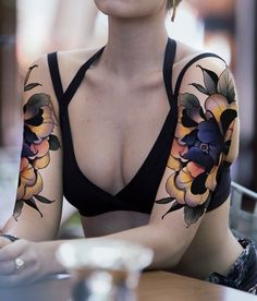 a woman sitting at a table with tattoos on her arms and chest, looking off to the side