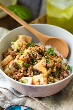 a bowl filled with rice, meat and veggies next to a wooden spoon