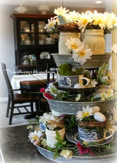 three tiered tray with flowers and teacups on the top, in front of a dining room table