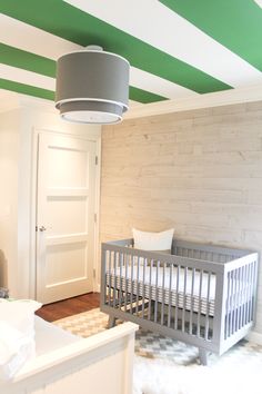 a baby's room with green and white stripes on the ceiling, crib in front