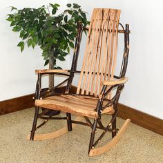 a rocking chair next to a potted plant on the floor in front of a white wall