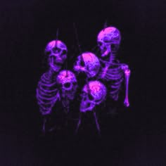 three skeletons in the dark with purple light on their faces and arms, all looking like they are holding hands together