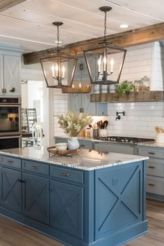 a large kitchen with blue cabinets and an island in the middle, surrounded by hanging lights