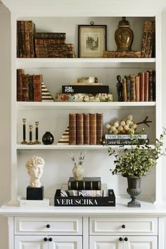 a white book shelf with books and vases on it's top, along with other decorative items