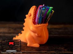 an orange dinosaur shaped pen holder with pens in it