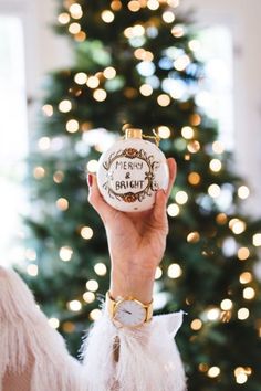 a person holding up a christmas ornament in front of a christmas tree