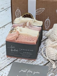 two soap bars sitting on top of a wooden table next to a card and bag