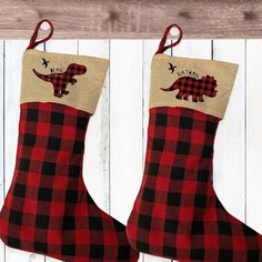 two red and black plaid christmas stockings hanging on a white wooden wall with an image of a dinosaur in the stocking