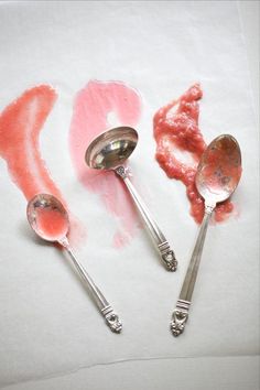 three spoons are sitting next to each other on a piece of paper with pink paint