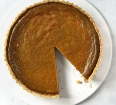 a pumpkin pie on a white plate with one slice missing from it's crust