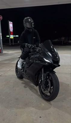 a man sitting on top of a black motorcycle in a parking lot next to a gas station