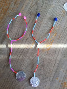 two necklaces made out of tinfoil and plastic beads on a wooden table next to a coin