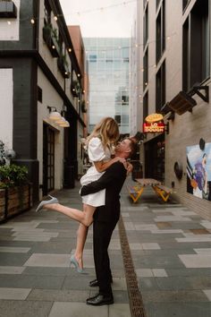 a man holding a woman on his back in an alleyway with buildings and string lights