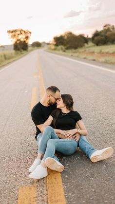 a man and woman sitting on the side of an empty road kissing in front of them