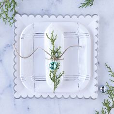 a white plate with green decorations on it and some greenery around the edge, sitting on a marble surface