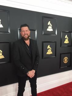 a man in black suit standing on red carpet next to wall with golden bell decorations