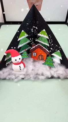 an origami house with snow and trees on the roof, surrounded by other decorations