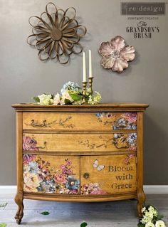 a dresser with flowers painted on it and two candles sitting on top of the drawers