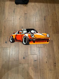 an orange and black car is on the floor next to a piece of wood that has been cut out