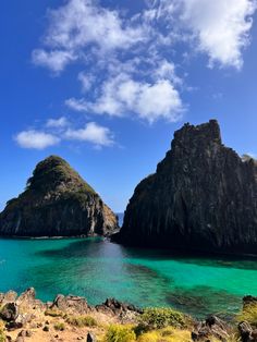 two large rocks sticking out of the ocean next to each other on a sunny day