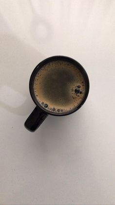 a black coffee cup sitting on top of a white table