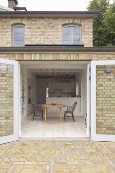 an open door leading to a kitchen and dining area with brick walls, white doors, and wooden chairs