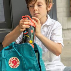 a young boy sitting on the ground with a backpack and water bottle in his hand