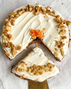 a carrot cake with white frosting and walnuts on top is cut into slices