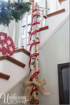 a christmas tree is tied to the bottom of a stair case with red and white twine