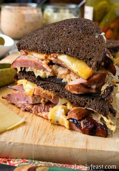 a sandwich with meat, cheese and other toppings sitting on a cutting board next to pickles