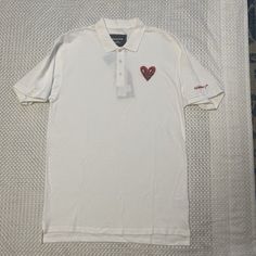 This Reason Clothing Polo Shirt Features An Embroidered Heart Design, Perfect For Any Occasion. The Shirt Is Made Of 100% Cotton And Has A Regular Fit, With Short Sleeves And A Collared Neckline. It Comes In Black And Is Available In Size L. The Shirt Is Machine Washable And Has Button Closure. It's Suitable For Various Activities Such As Tennis, Walking, School, Golf, Dance, Driving, And Fishing. The Shirt Is Part Of The Keith Haring Product Line And Is Perfect For Men Who Want To Make A Statem Casual Embroidered Collared Tops, Embroidered Cotton Collared Tops, Casual Polo T-shirt With Embroidered Logo, Casual Collared T-shirt With Embroidered Logo, Casual Embroidered Polo Collar Top, White Embroidered Heart-shaped Top, White Embroidered Tops With Heart Design, Fitted Embroidered Short Sleeve Polo Shirt, Embroidered Cotton Polo Collar Tops