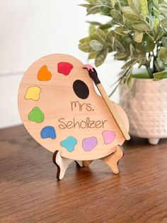 a wooden plate with paintbrushes on it and a potted plant in the background