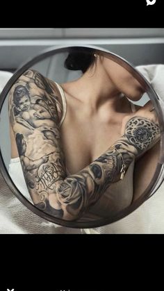 a woman with tattoos on her arm is looking in the mirror and holding it up to her chest